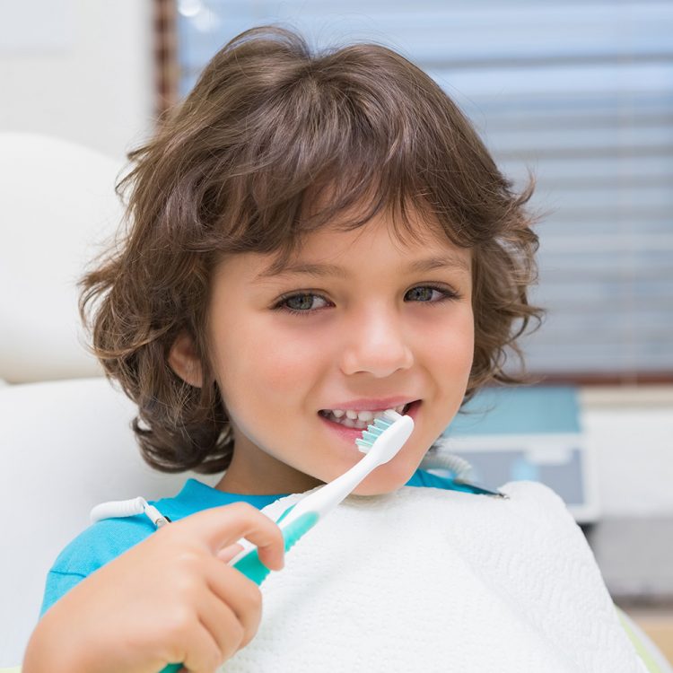 A young child brushing his teeth in the dental chair